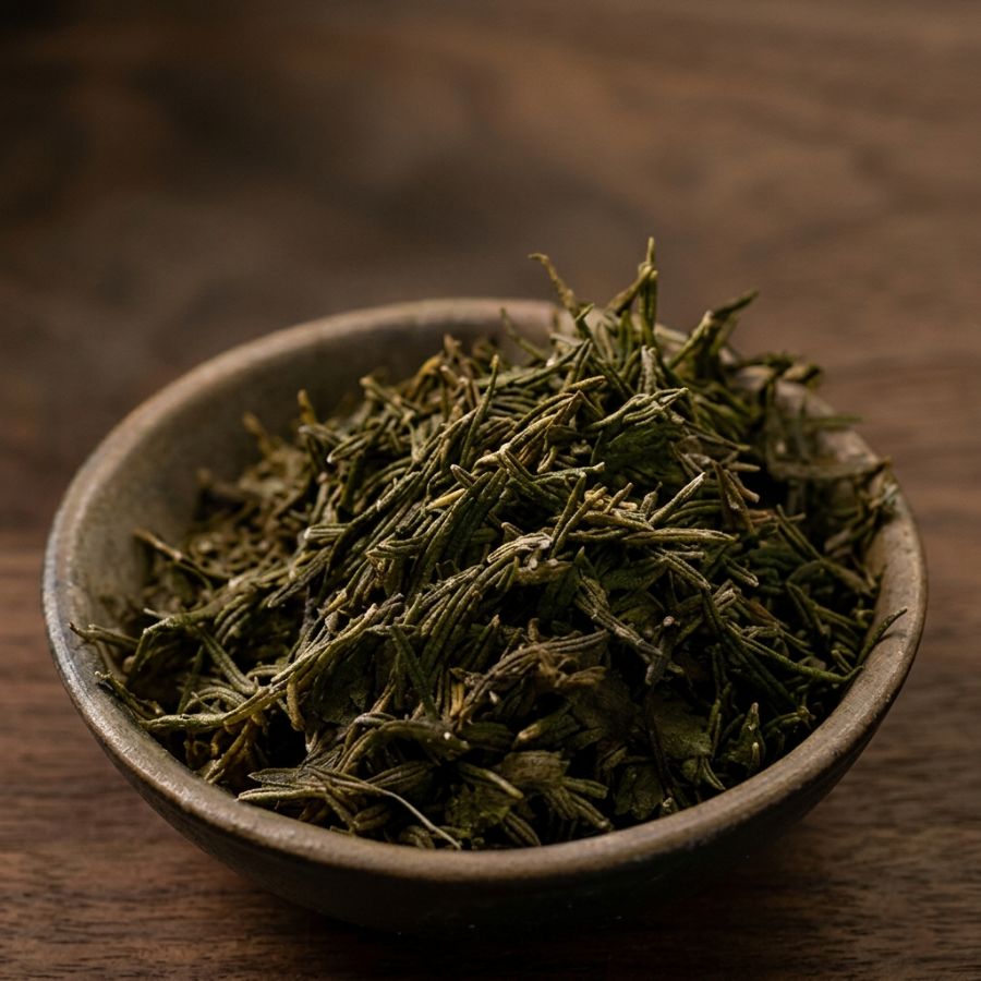 Dried green tea leaves in a ceramic bowl on a wooden surface