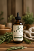 Bottle of Valor Herb Co. rosemary hair oil on a wooden surface with greenery.