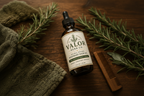 Bottle of Valor Herb Co. Rosemary Hair Oil on a wooden surface with rosemary branches and a comb.